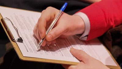 close up of person in red sweater completing a survey on a clipboard