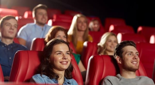 A group of young people sit in red theatre seats, smiling at a performance. 