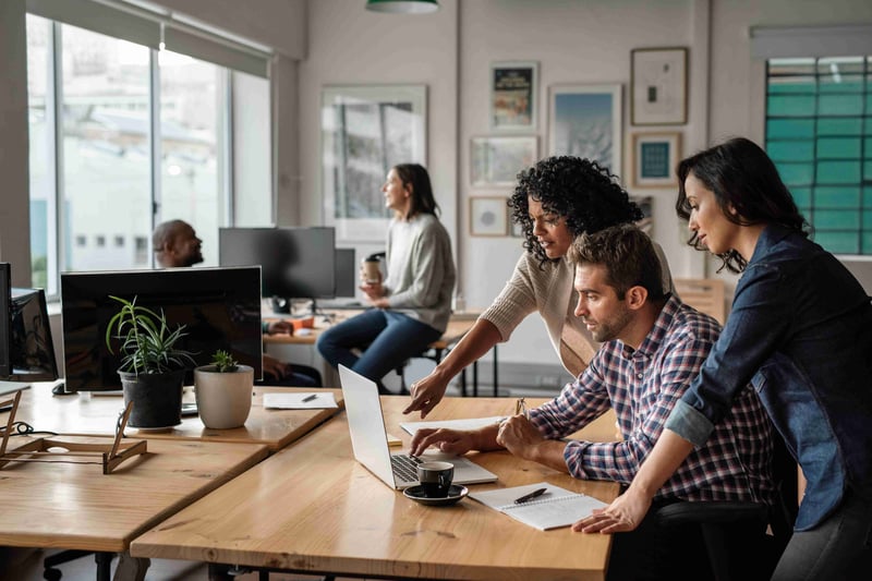 Three coworkers collaborate on a project, looking at a laptop screen together.