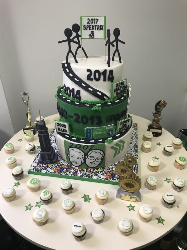 Large 3 tiered green and white cake with travel lanes and chevrons surrounded by cupcakes