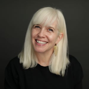 Brooke smiles, wearing a black shirt and gold earrings.