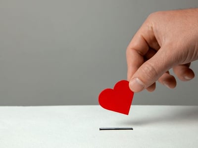 A hand places a red paper heart into a coin slot