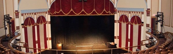 View from the circle of the Grand Opera House, looking at a dark stage beneath a red-gold fringed curtain