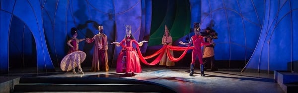 A queen in a red dress and crown is surrounded by courtiers onstage at Contemporary American Theatre Festival