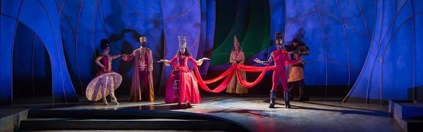 A queen in a red dress and crown is surrounded by courtiers onstage at Contemporary American Theatre Festival