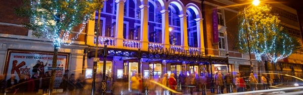 The exterior of Wolverhampton Grand Theatre at night, with a crowd gathered in front of an arched facade lit in blue