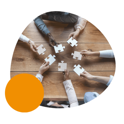 multiple hands holding puzzle pieces at a wooden table