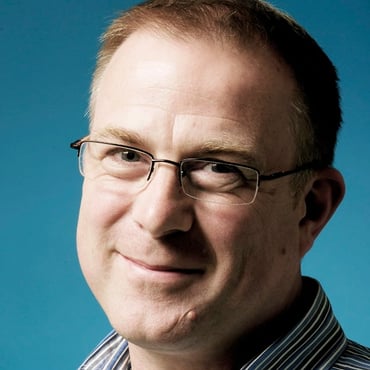 Andrew McIntyre wears glasses and smiles in front of a blue background.
