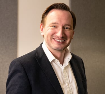 Robin Cantrill-Fenwick, a white man with brown hair wears a white collared shirt and a black jacket and smiles