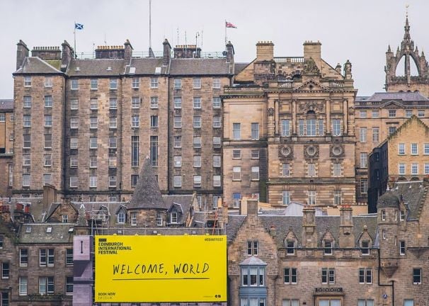 The Edinburgh skyline, with a large yellow banner reading 'Welcome, World'