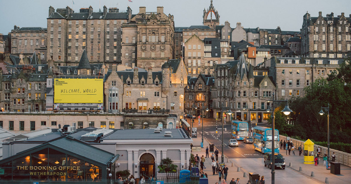 Edinburgh rooftops during the International Festival, with a large yellow poster reading Welcome World