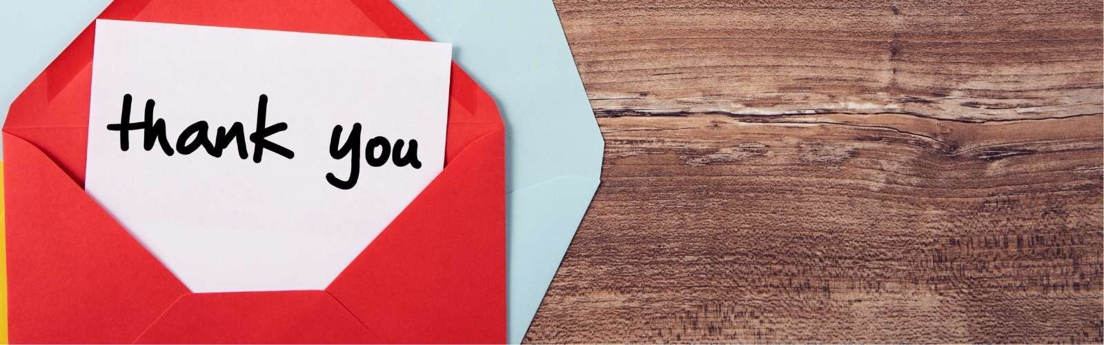 hand written thank you in a red envelope on a wood background