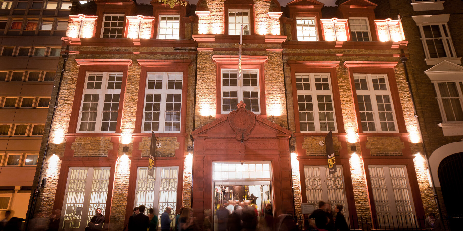 People gather outside The Place, a beautiful brick venue in London, at night.