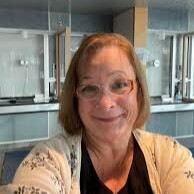 Cate Foltin, Business manager of Macomb Center for the Performing Arts, wears a white cardigan, a black shirt, and red glasses.