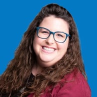 Cheyenne Queen, Patron Services Manager at Music Theatre Wichita, wears blue classes and smiles against a blue backdrop.
