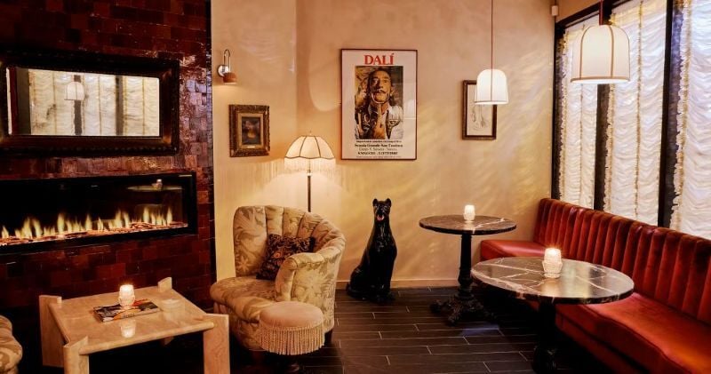 The interior of Club X Speakeasy in Chicago, Illinois, featuring a red velvet couch, marble tables, a Dali picture, and a sculpture of a dog.