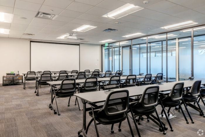 A meeting room with chairs, desks, and a projector screen inside Venture X in Denver, Colorado.