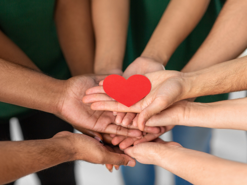 an image of different hands holding a red paper heart