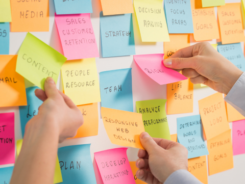an image of hands arranging sticky notes on a white board