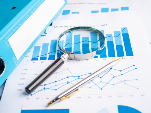an image of a magnifying glass laid over paper with blue graphs and data on it