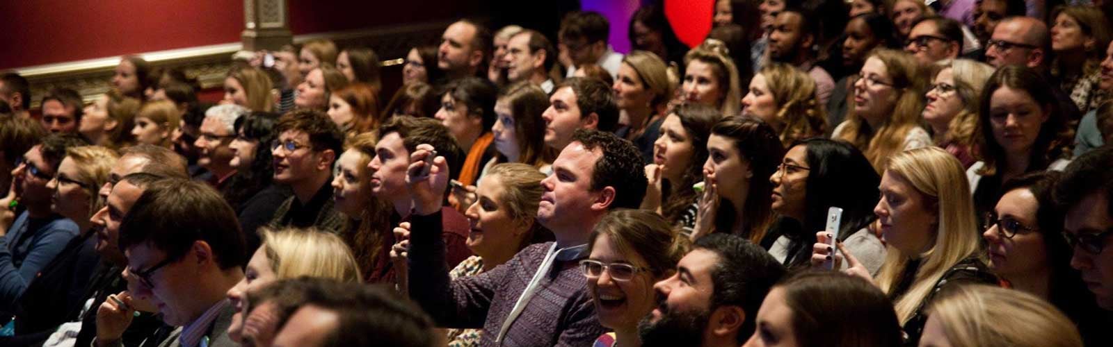An audience of conference attendees listens to a talk