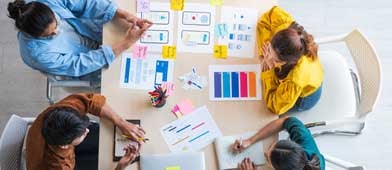 Four people sitting at a desk reviewing colorful analytics paperwork