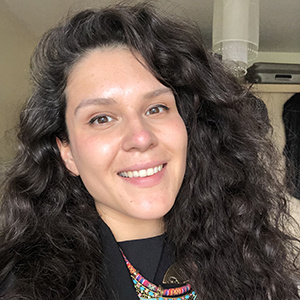 A headshot of Pam Garratt, a woman with dark curly hair, wearing a dark shirt and smiling into the camera