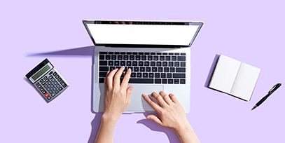 Hands at a laptop next to a calculator and notebook