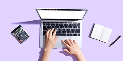 Hands at a laptop next to a calculator and a notebook