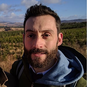 A headshot of Paul McGuinness, a man with dark hair and a beard, wearing a green jacket.