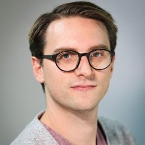 A headshot of Tom Nolan, a male with brown hair and glasses.