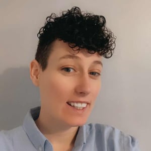 A headshot of Jade Walton, a woman with dark curly hair, wearing a blue shirt and smiling at the camera.