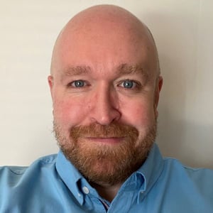 Niall Palmer wears blue button down in front of a beige background