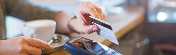 a person tapping their debit card on a card reader next to a cup of coffee