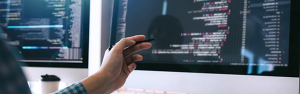 a hand with a pen pointing at code on two screens