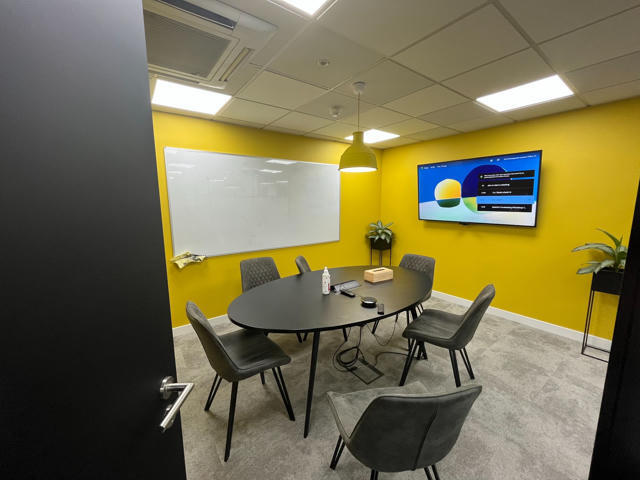 The Cheesegrater meeting room in the Spektrix office in London, featuring yellow walls, a whiteboard, and a meeting table.