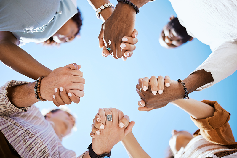 multiple people holding hands together under a blue sky