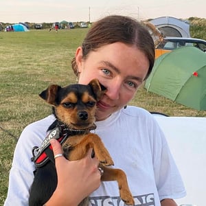 Grace Plumb, a white woman with brown hair tied up, showcasing her little black & tan dog on a Welsh campsite