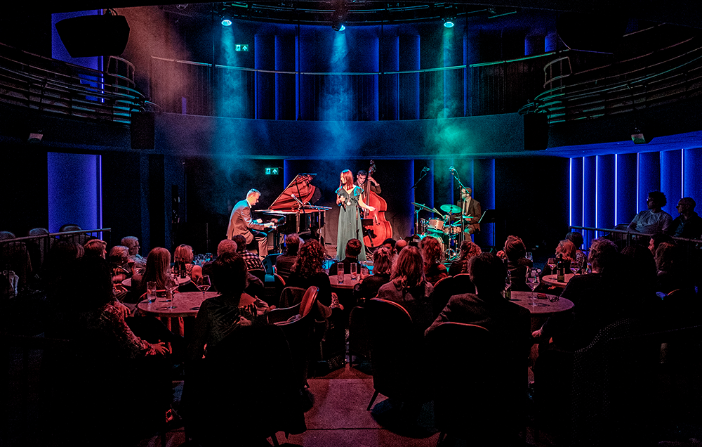 Musicians onstage at Boulevard Theatre, with the audience seated on cabaret tables around them