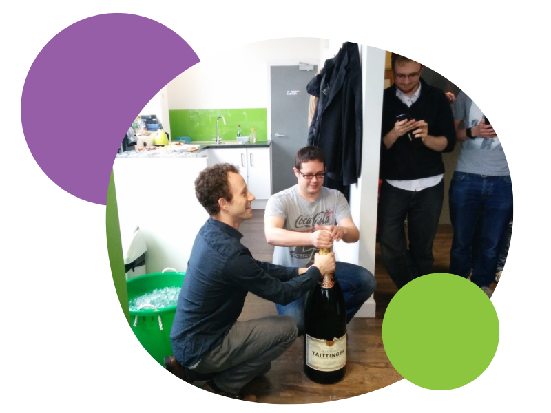 An extraordinarily large bottle of champagne is opened on the floor of the first Spektrix office. Green walls abound.