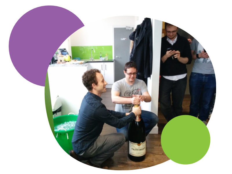 An extraordinarily large bottle of champagne is opened on the floor of the first Spektrix office. Green walls abound.