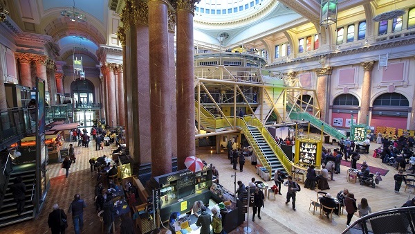 The busy foyer of the Royal Exchange Theatre, housing a modern yellow theatre module inside an historic hall made of pink marble