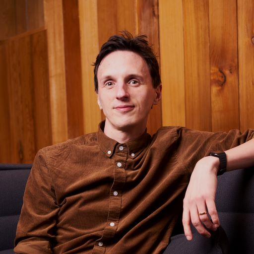 James Akers a white man with dark brown hair wearing a brown shirt sitting in front of a wooden backdrop
