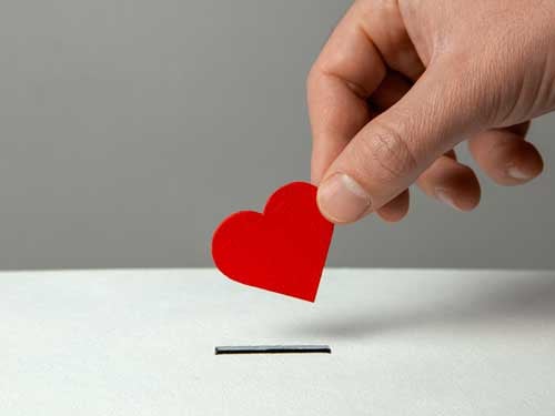 A hand putting a paper heart in a coinslot.