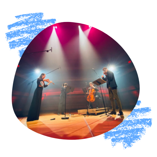A string quartet stand onstage at the Isabel Bader Centre for the Performing Arts, silhouetted under bright lights