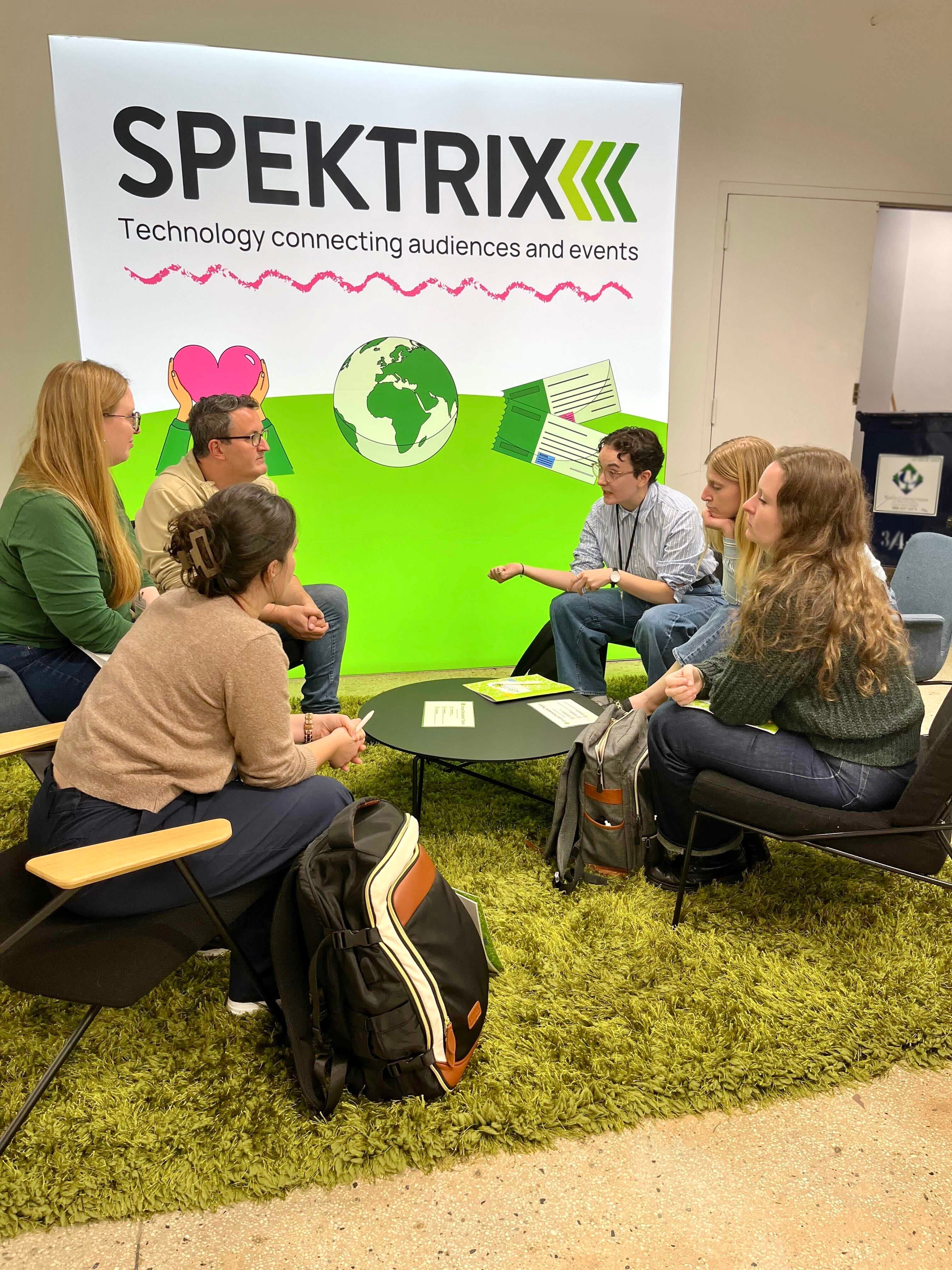 A group of arts professionals are deep in discussion in front of a glowing Spektrix banner