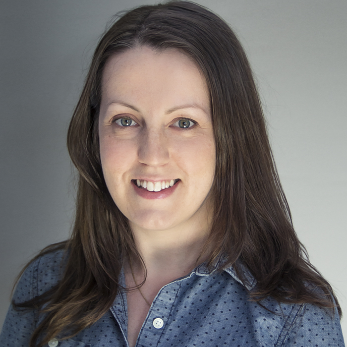 A headshot of Jane Whitty, a white woman with long brown hair, wearing a blue collared shirt.