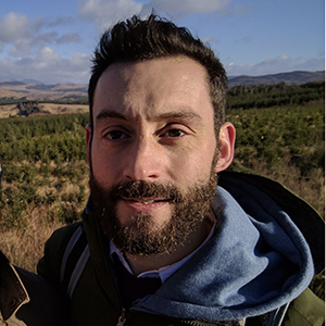 A headshot of Paul McGuinness, a man with dark hair and a beard, wearing a green jacket.