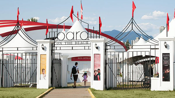 Front entrance to Bard on the Beach, a city of white turreted marquees with red flags waving in the breeze