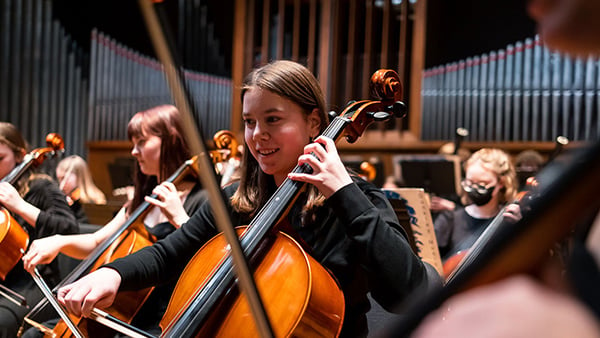A smiling cello player performs in an orchestra at Boise Philharmonic